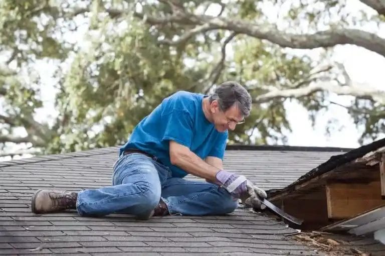 A man removing rotten wood from his roof caused by an ice dam in the winter months.