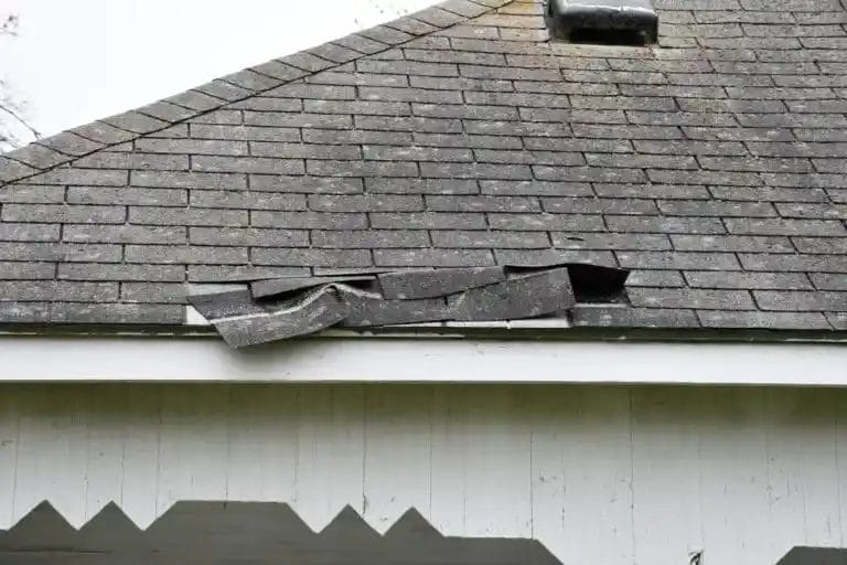 A wind damaged roof with shingles lifted up on the edge.