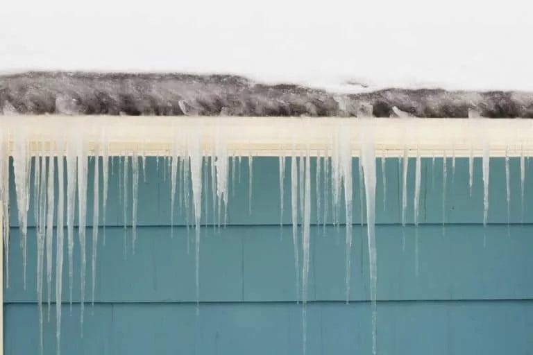 An ice dam on a gutter of a house. Ice dams are a sign of winter roof damage.