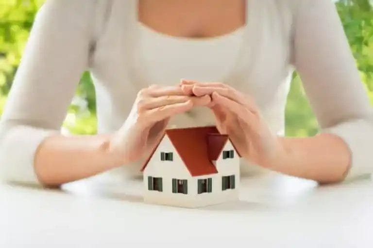 A woman holding her hands to protect and cover a model house.