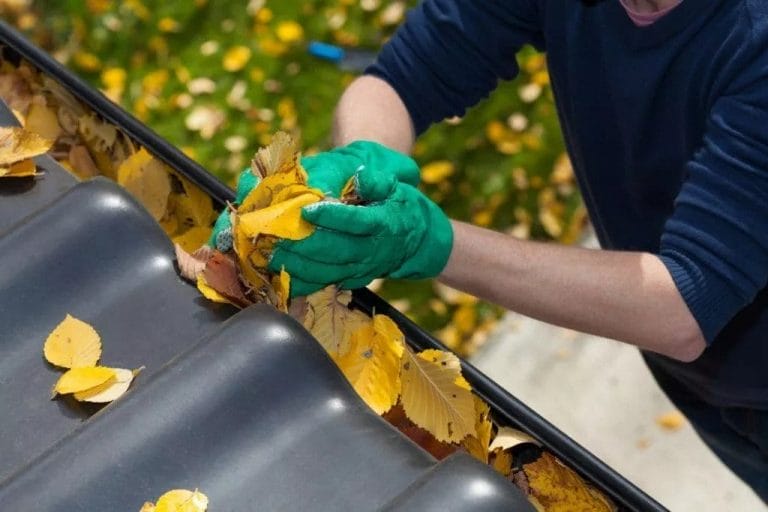 Someone cleaning out a rain gutter. Proper gutter installation with precautionary measures can help limit how often gutters need to be cleaned.